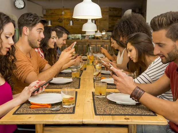 people seated at dinner all look at their cellphones